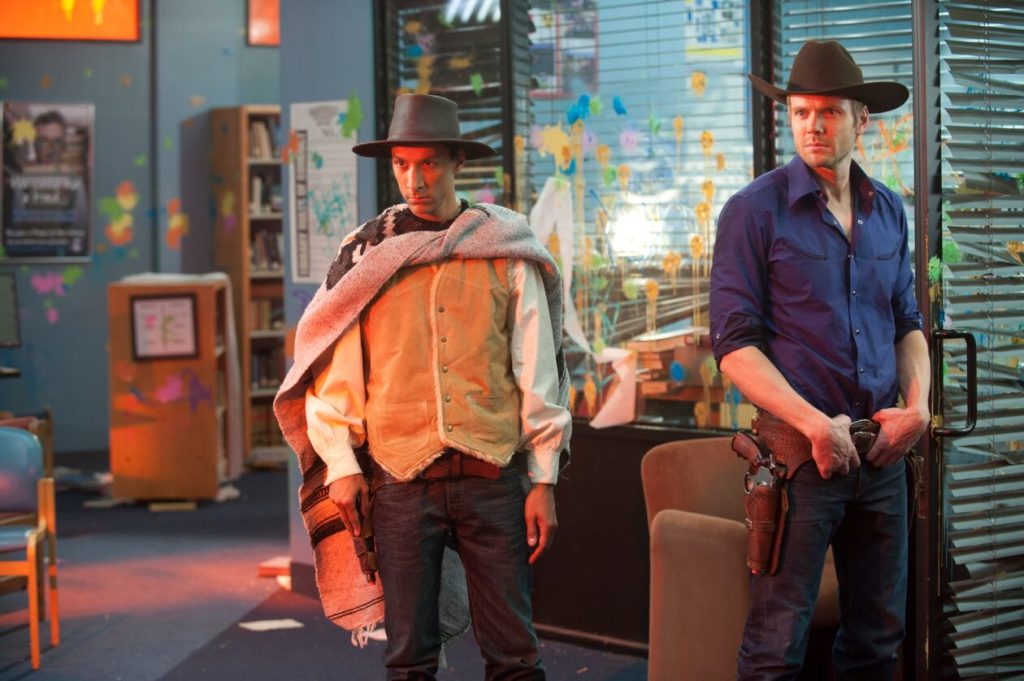 Abed und Jeff stehen in Cowboy-Kostümen in dem, von der Paintballschlacht gezeichneten, Gruppenarbeitsraum.