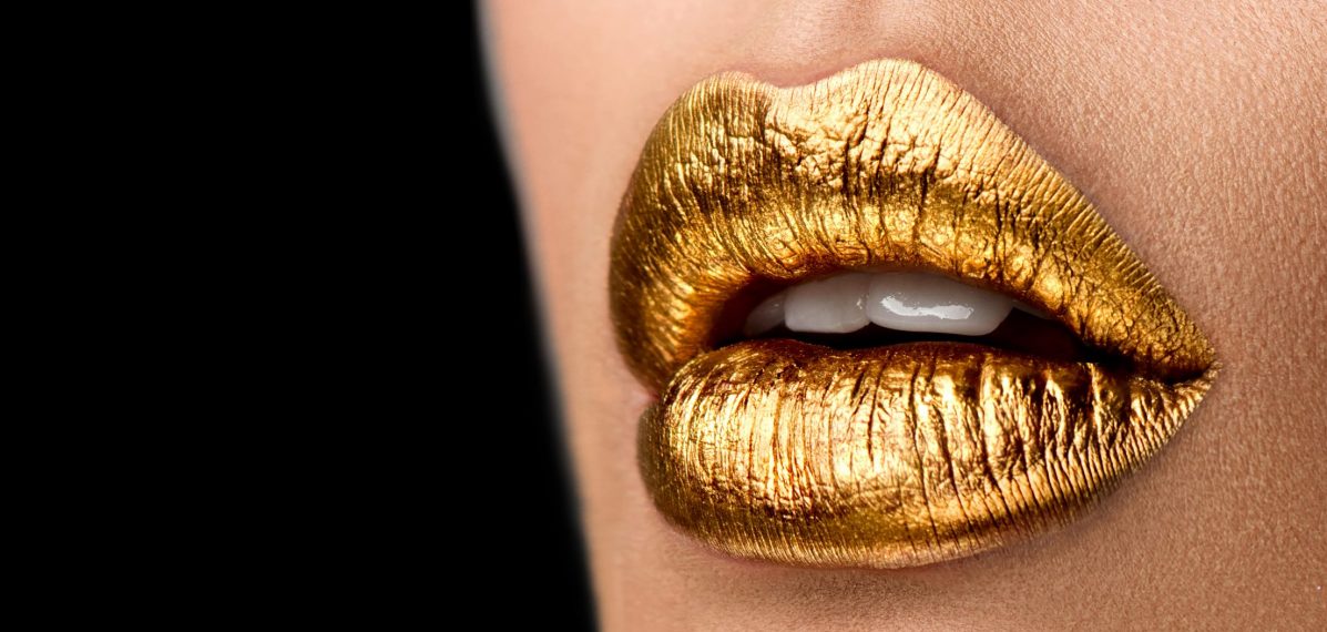 Eine Nahaufnahme von den Lippen einer Frau, sie trägt goldenen Lippenstift