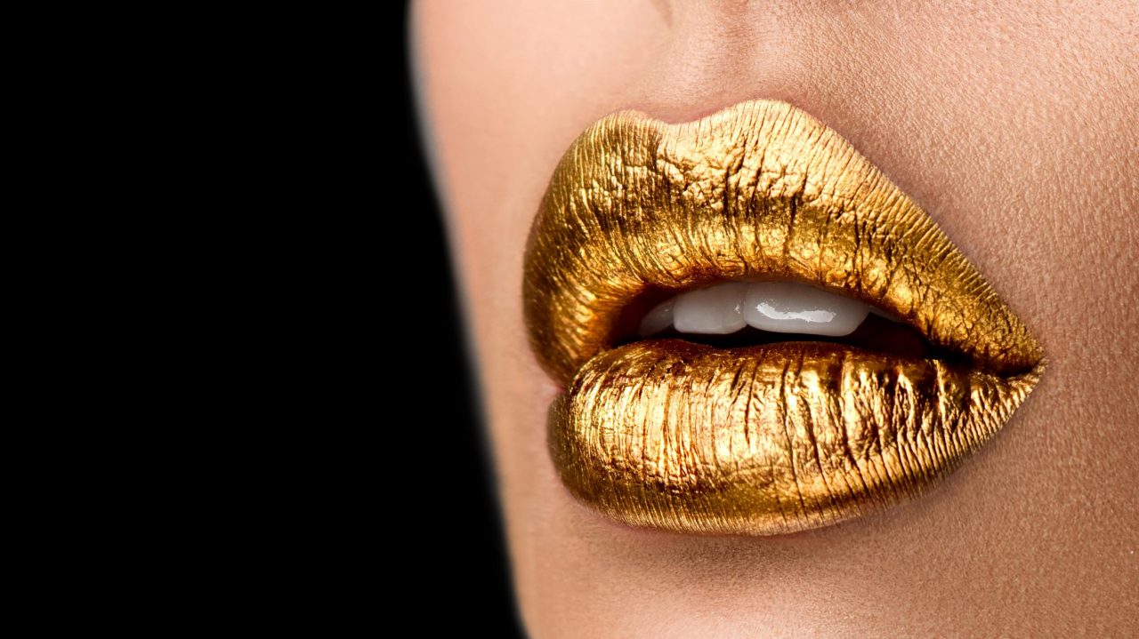 Eine Nahaufnahme von den Lippen einer Frau, sie trägt goldenen Lippenstift