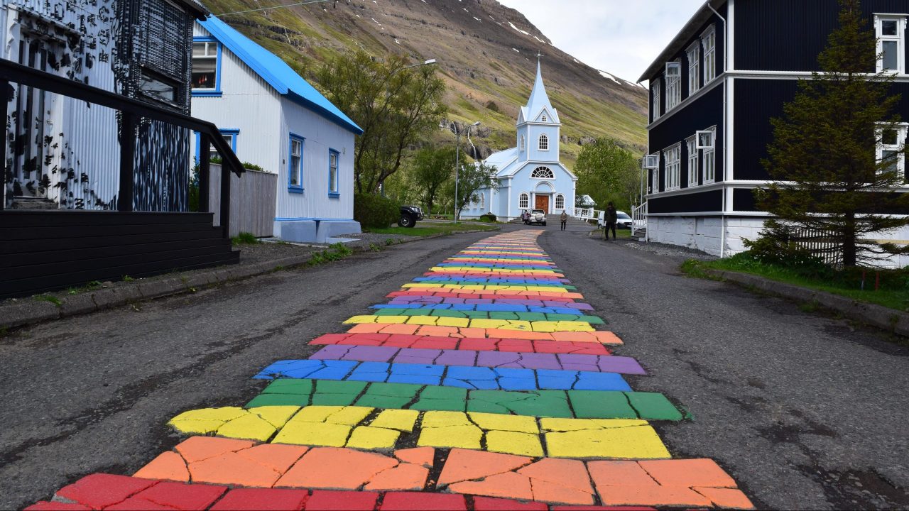 Ein Regenbogenweg in einer Kleinstadt der zu einer kleinen Kapelle aus Holz führt.