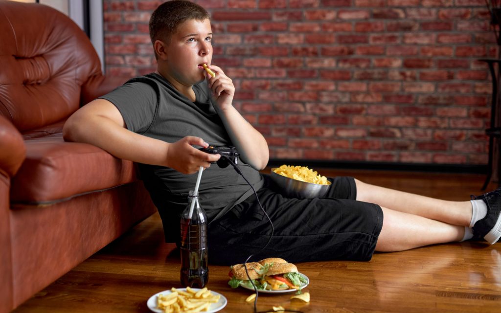 Ein Junge isst Fast Food und lümmelt vor dem Sofa
