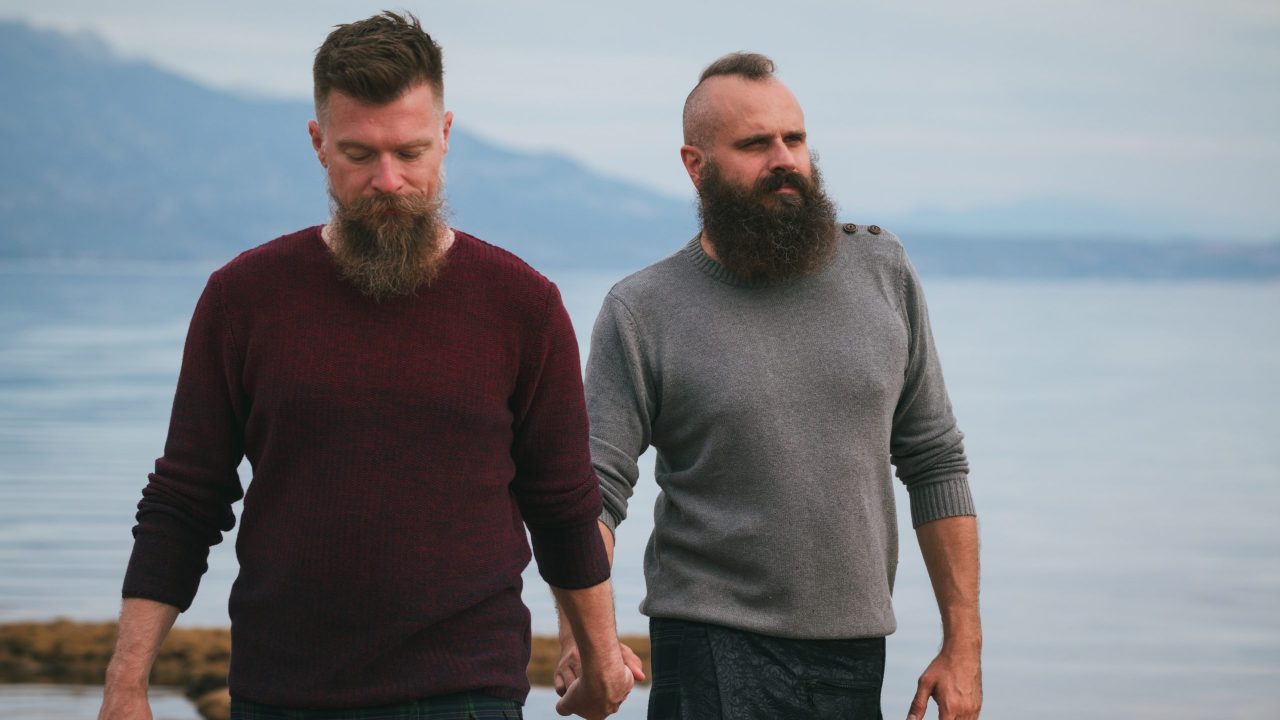 Zwei heterosexulle Männer spazieren gemeinsam am Strand.